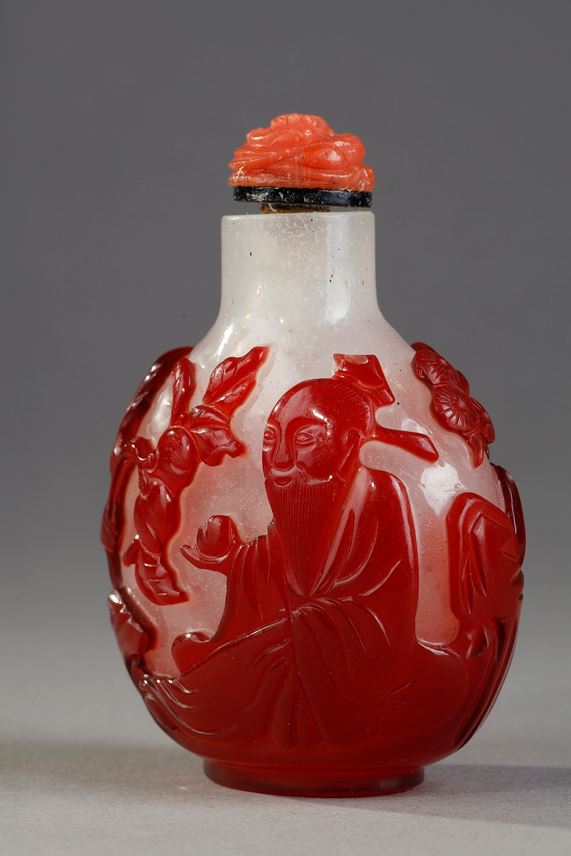 Snuff bottle  red overlay glass with Shou Lao holding a peche of longevity and looking at peches and on the other side of a character holding a cup on a tray in front of a pine - China 1800/1850 | MasterArt
